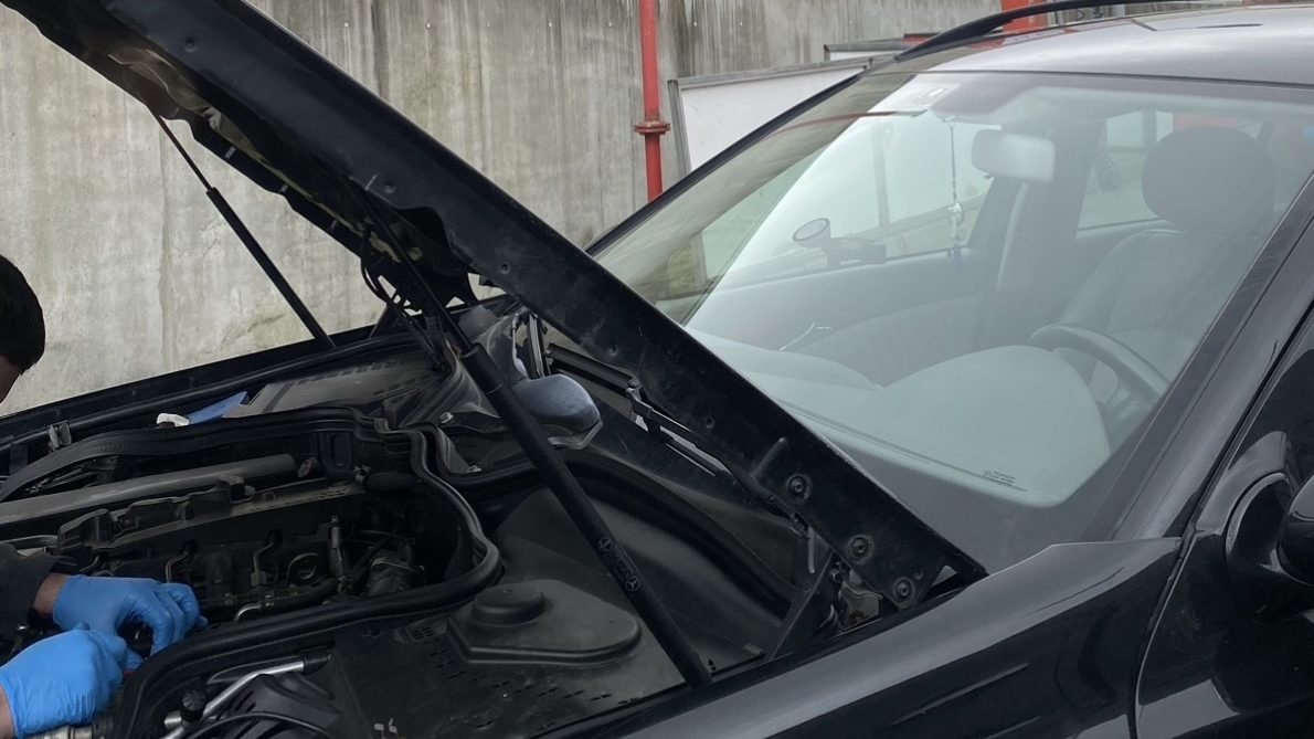 Arbeit am geöffneten Motorraum eines Fahrzeugs, Hände in Arbeitshandschuhen